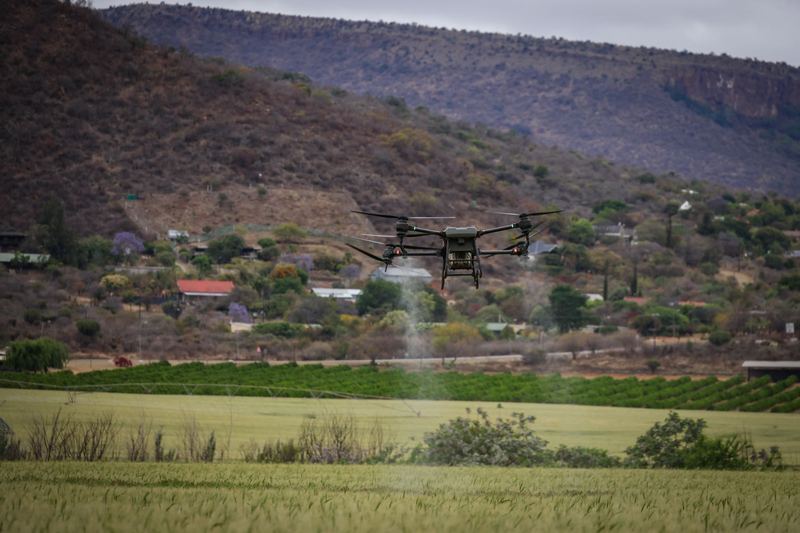 Agricultural drone spraying a paddock near a farm settlement at the foot of a range