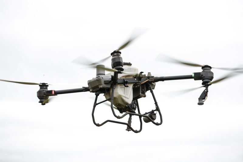 Large agricultural spray drone in flight showing its tank, rotors and spray nozzles