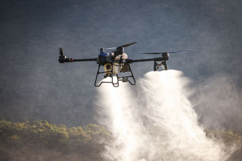 Agricultural spray drone releasing two wide plumes of spray over a paddock